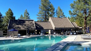 Une piscine entourée d’arbres et d’un bâtiment au toit en pente, avec des chaises longues et des parasols à proximité.