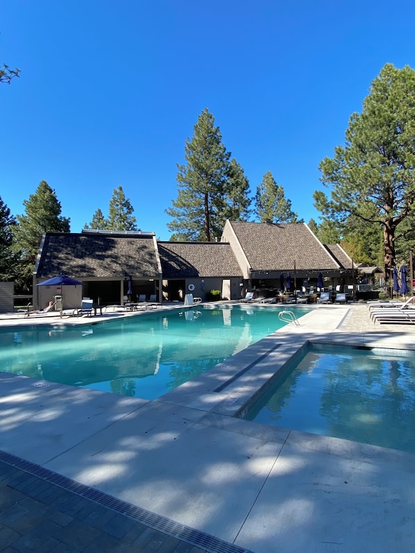 Une piscine entourée d’arbres et d’un bâtiment au toit en pente, avec des chaises longues et des parasols à proximité.
