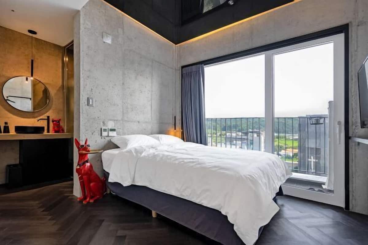 Un dormitorio moderno con una cama grande, un espejo redondo, un escritorio pequeño y una estatua de perro rojo.