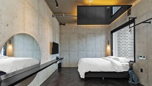 A modern hotel room with a large bed, a bench, a TV, and a window with blinds. - Ingu Stay (Yangyang)