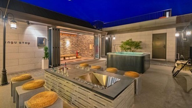 A modern outdoor kitchen area with a stone wall, a bar counter, and seating with woven stools. - Ingu Stay (Yangyang)