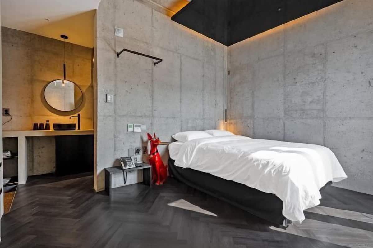 Un dormitorio moderno con una cama, un espejo redondo, una escultura roja y un escritorio pequeño.