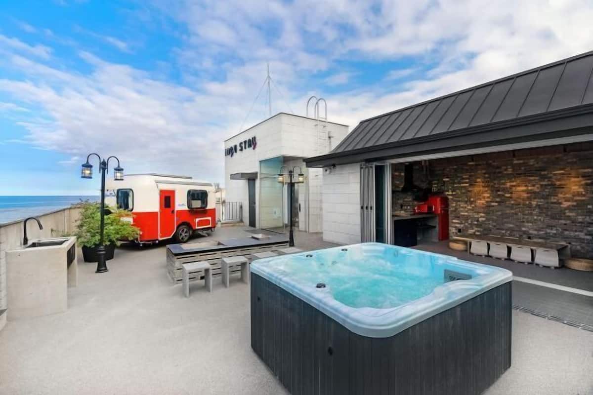Un jacuzzi, zona de estar al aire libre, una caravana roja y blanca, y un edificio con un letrero.