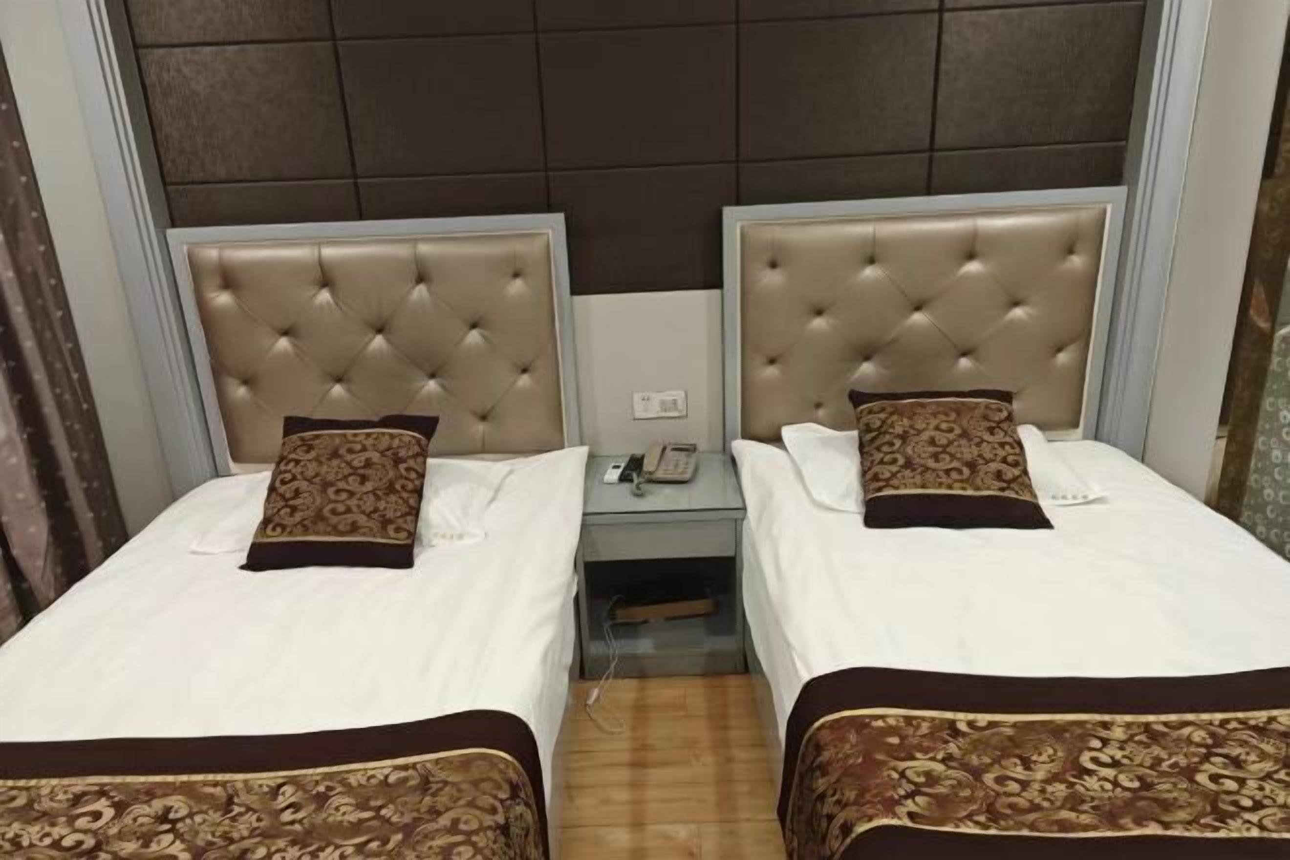 A hotel room with two beds, each with a tufted headboard, a bedside table with a phone, and a patterned bedspread.