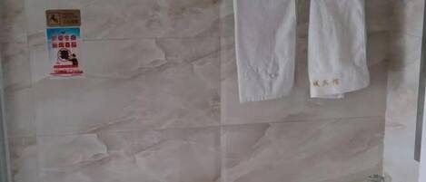 Un baño con inodoro, lavabo y un perchero para toallas. Hay un cartel en la pared y una bandeja amarilla con artículos de aseo.