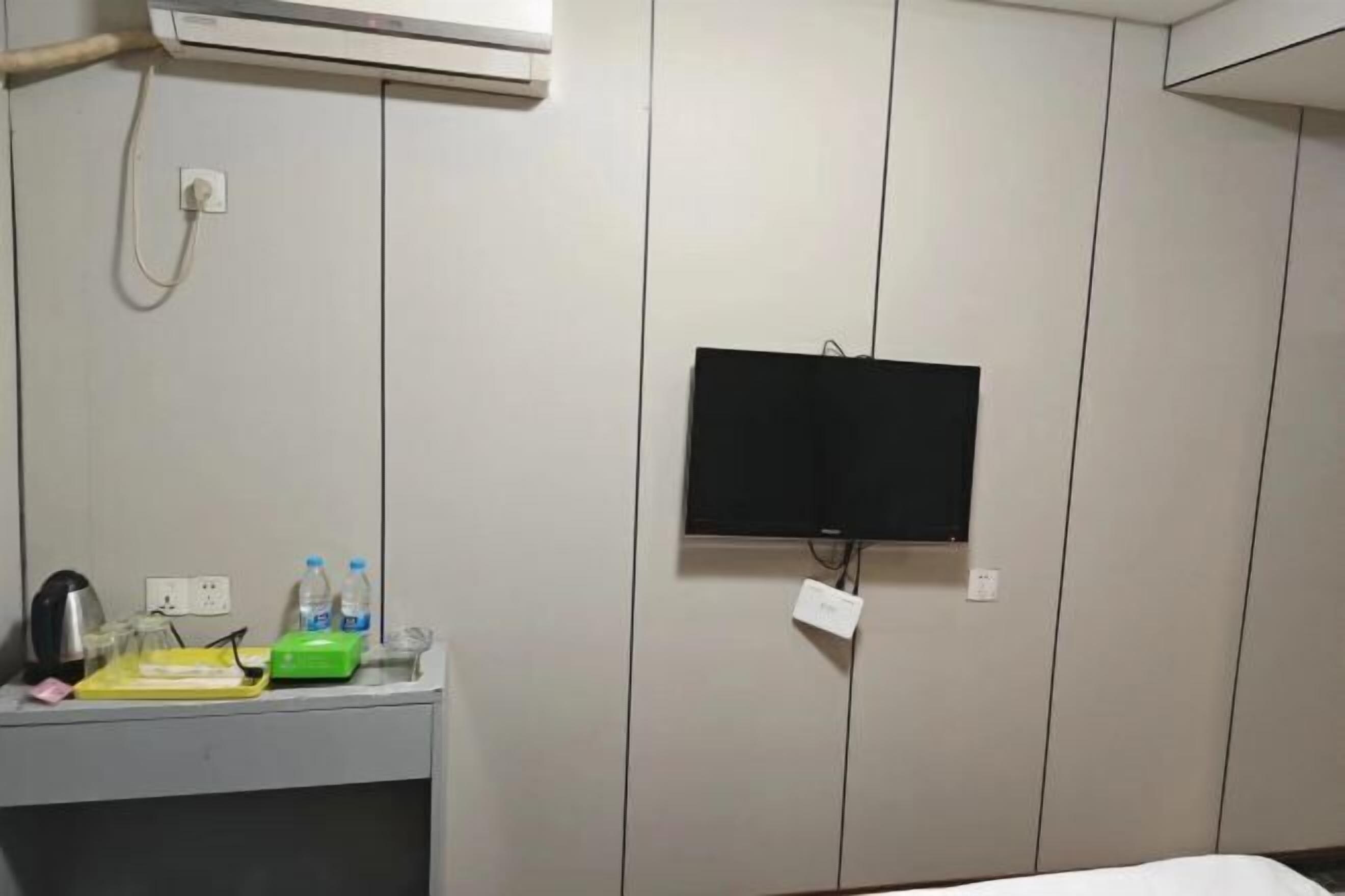 Habitación de hotel con televisor de pantalla plana montado en la pared, una mesita con hervidor, botellas de agua y una caja verde.