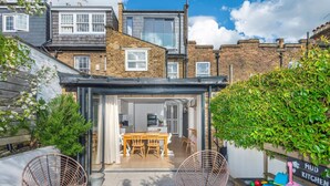 A modern house with a patio area featuring a dining table and chairs, a small kitchen area, and a seating area with a hammock and a flamingo-shaped pillow. - 3-bedroom Home in Richmond - Ideal Family Living (London)