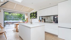 A modern kitchen with white cabinetry, a central island, and a view of a garden through large windows. - 3-bedroom Home in Richmond - Ideal Family Living (London)