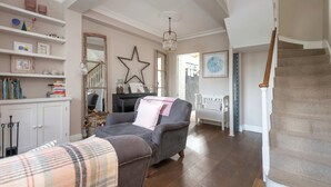 A spacious living room with a grey armchair, a white sofa, and a wooden staircase. - 3-bedroom Home in Richmond - Ideal Family Living (London)