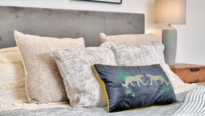 A bed with beige pillows, a black pillow with a golden animal design, a grey lamp, and framed artwork on the wall. - Stunning Apartment in the Heart of Chelmsford (Chelmsford)