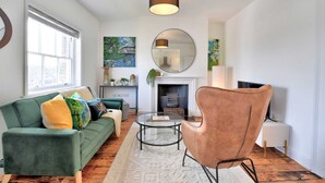 A living room with a green sofa, a round leather chair, a glass coffee table, a fireplace, and a large mirror on the wall. - Stunning Apartment in the Heart of Chelmsford (Chelmsford)