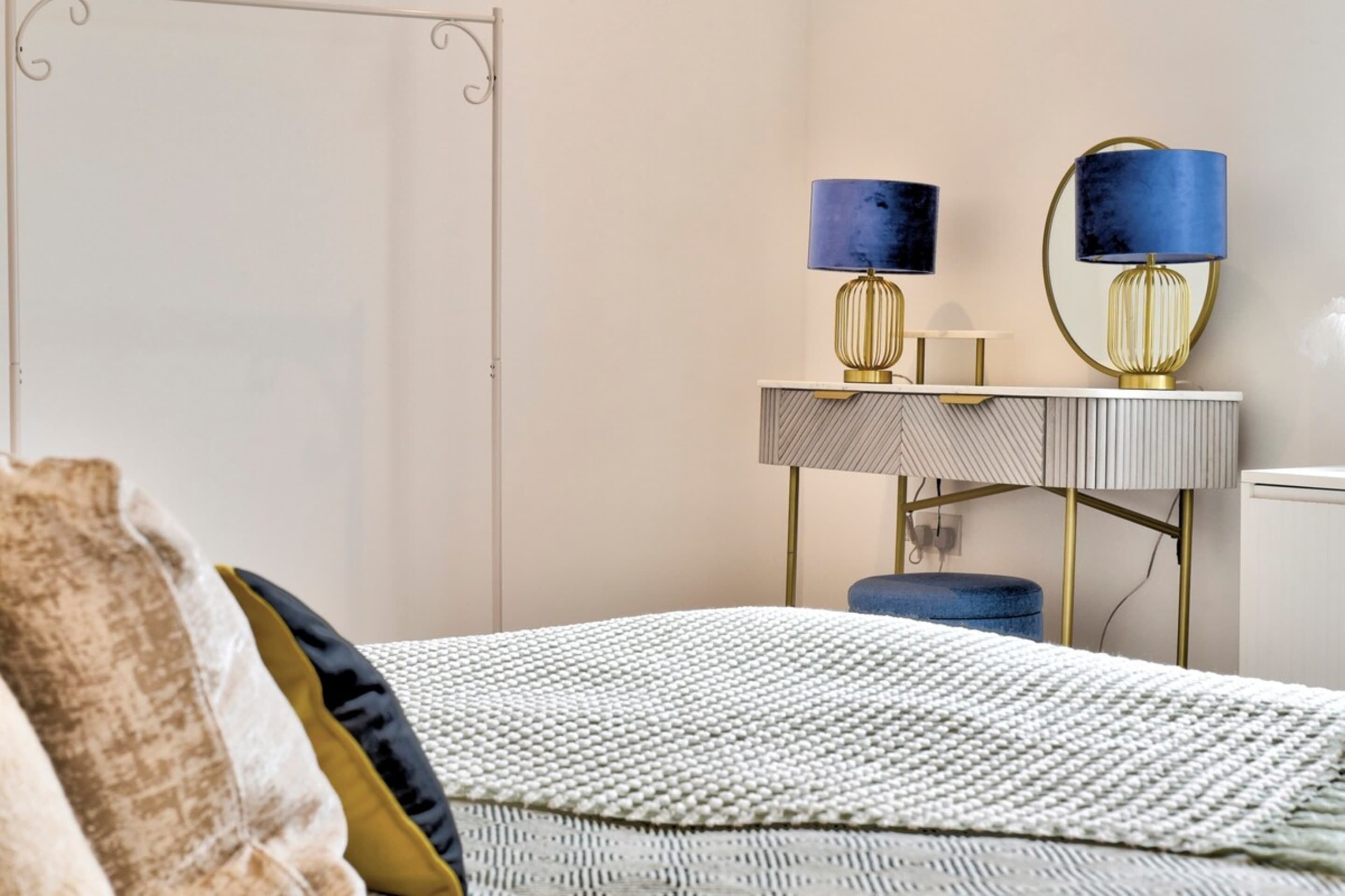 A bedroom with a bed, a bedside table with lamps, and a mirror.