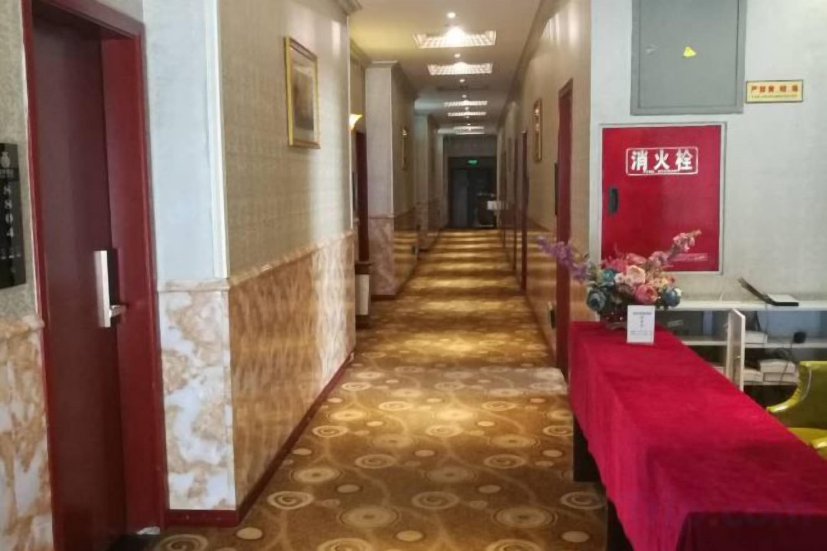 A hotel corridor with a patterned carpet, a red carpeted table, and a fire safety sign.