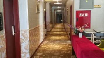 A hotel corridor with a patterned carpet, a red carpeted table, and a fire safety sign.