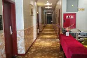 Ein Hotelgang mit einem gemusterten Teppich, einem mit rotem Teppich ausgelegten Tisch und einem Brandschutznachweis.