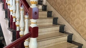 Un escalier avec des balustrades blanches et des rampes rouges, menant à un palier orné d’un mur à motifs.