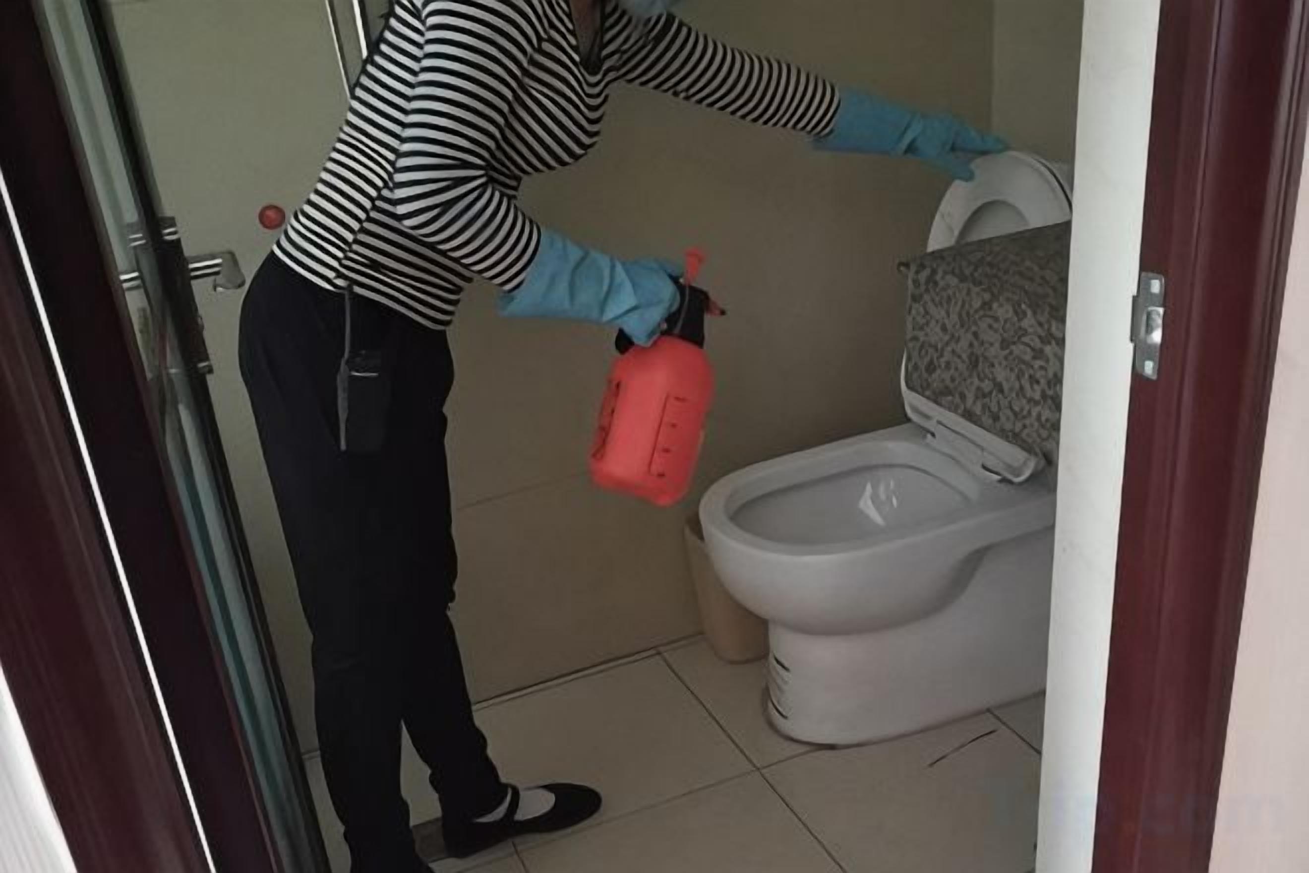 A person cleaning a toilet with a spray bottle.
