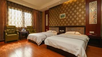 A hotel room with two beds, a green armchair, a small table, and a decorative wall.