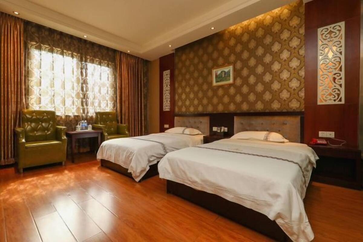 A hotel room with two beds, a green armchair, a small table, and a decorative wall panel.