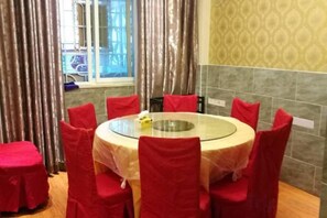 A round table with a glass top surrounded by red chairs, set against a patterned wall and a window with curtains. - Panzhihua Kaidikangyang Hotel (Panzhihua)