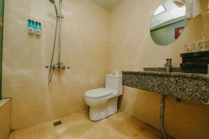 Un baño con inodoro, ducha, lavamanos de encimera de granito y espejo.