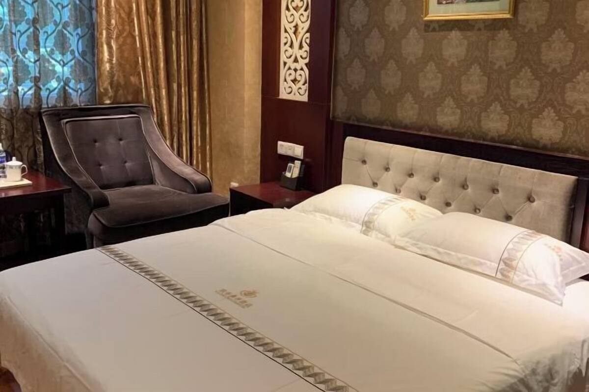 A hotel room with a large bed, a chair, a nightstand, and a decorative wall panel.