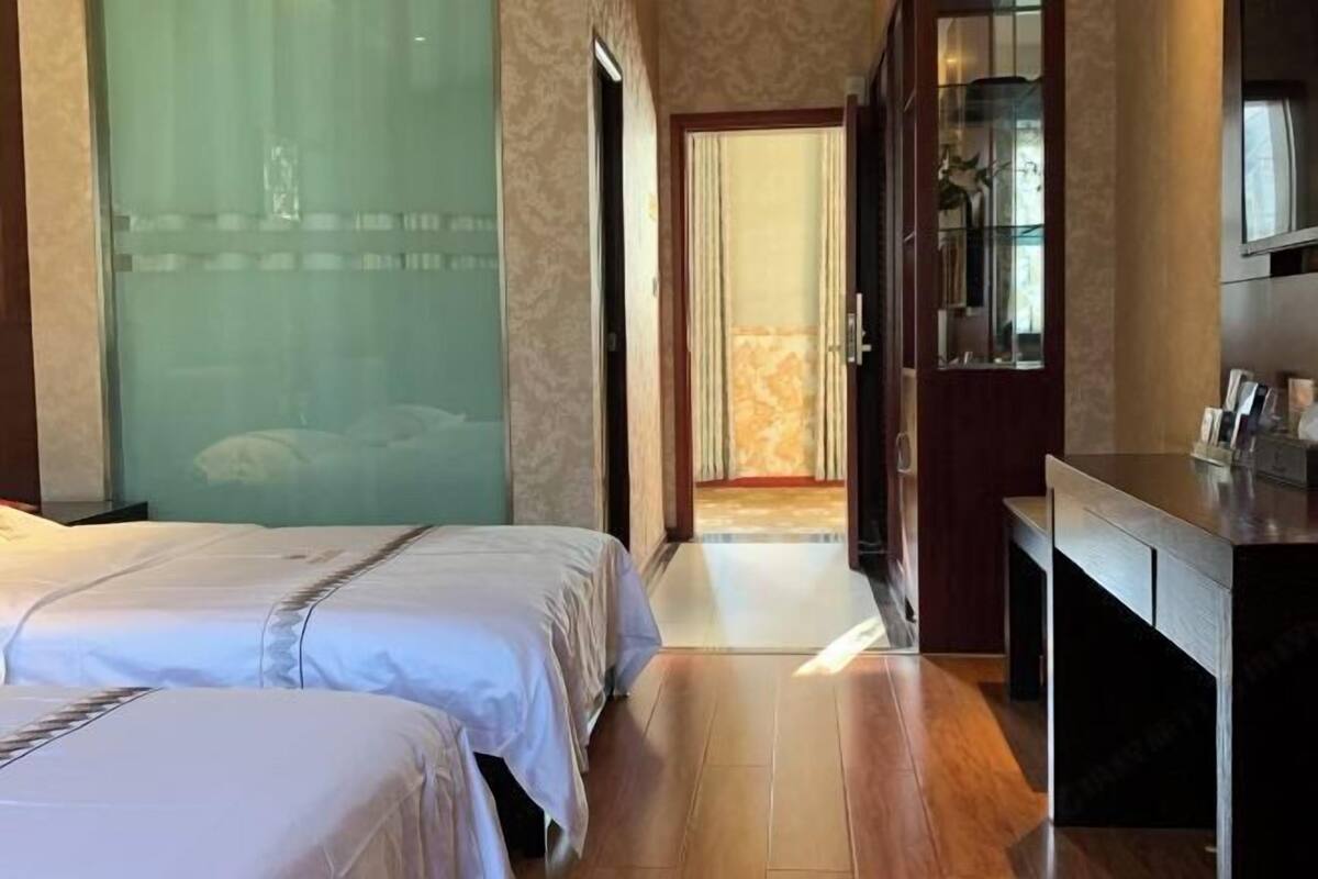A hotel room with two beds, a wooden floor, a mirror, and a door leading to another room.
