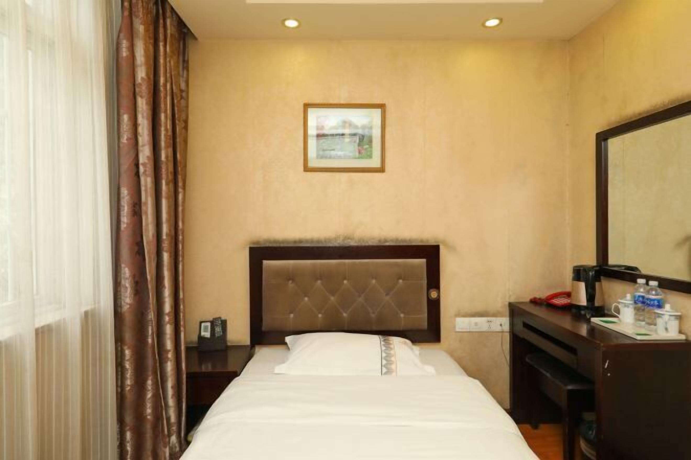 Ein Hotelzimmer mit einem Bett, einem Nachttisch, einem Schreibtisch, einem Stuhl, einem Spiegel und einem Fenster mit Vorhängen.
