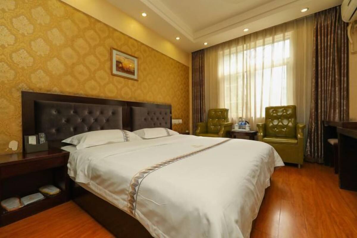 A hotel room with a large bed, wooden floor, a nightstand with a lamp, and a chair.