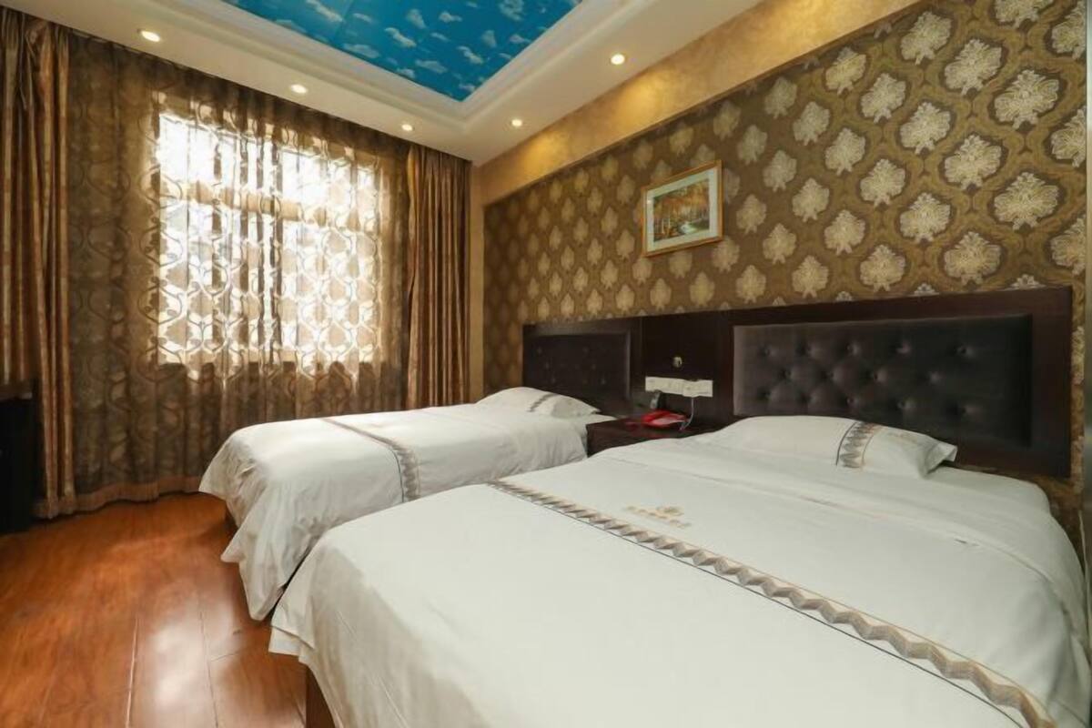 A hotel room with two beds, a ceiling with a blue pattern, patterned wallpaper, and a framed picture on the wall.