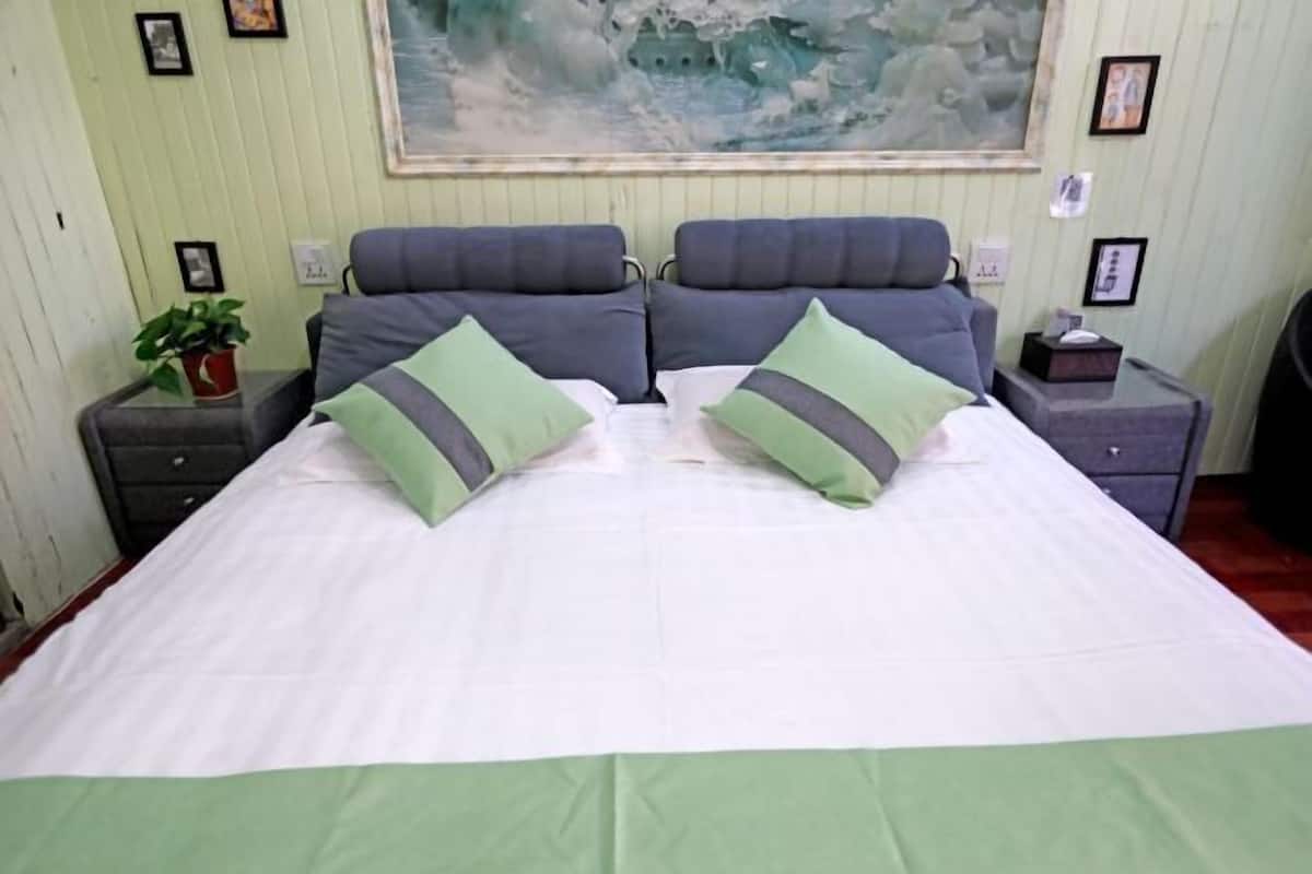 A bed with a white and green bedspread, two gray pillows, and a painting above.