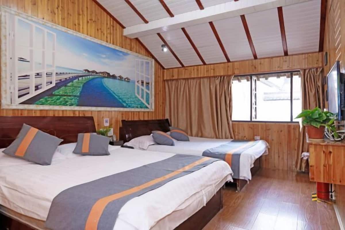 A wooden-paneled room with two beds, a large window with curtains, and a painting of a coastal scene.