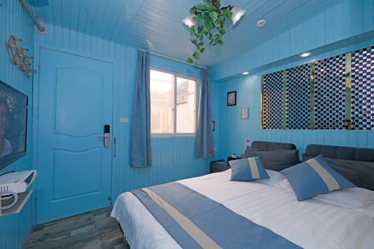 A room with a large bed, a window with curtains, a checkered wall, and a plant hanging from the ceiling.