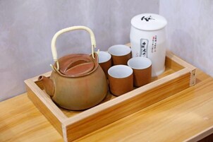Una bandeja de madera con una tetera de arcilla, varias tazas marrones y un recipiente blanco con tapa.