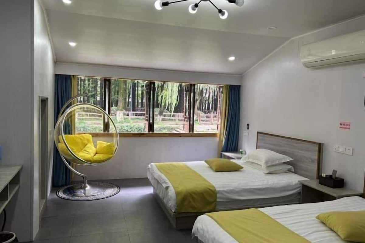 A hotel room with two beds, a hanging chair, and a window with a view of greenery.