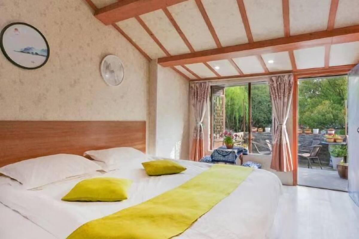 A bedroom with a bed, a fan, and a view of an outdoor patio with chairs and plants.