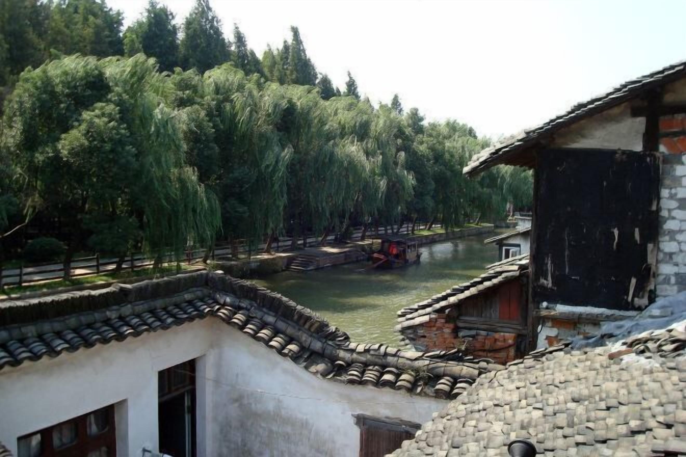 A traditional building with a tiled roof, a stone wall, and a wooden structure adjacent to a waterway with a bridge.