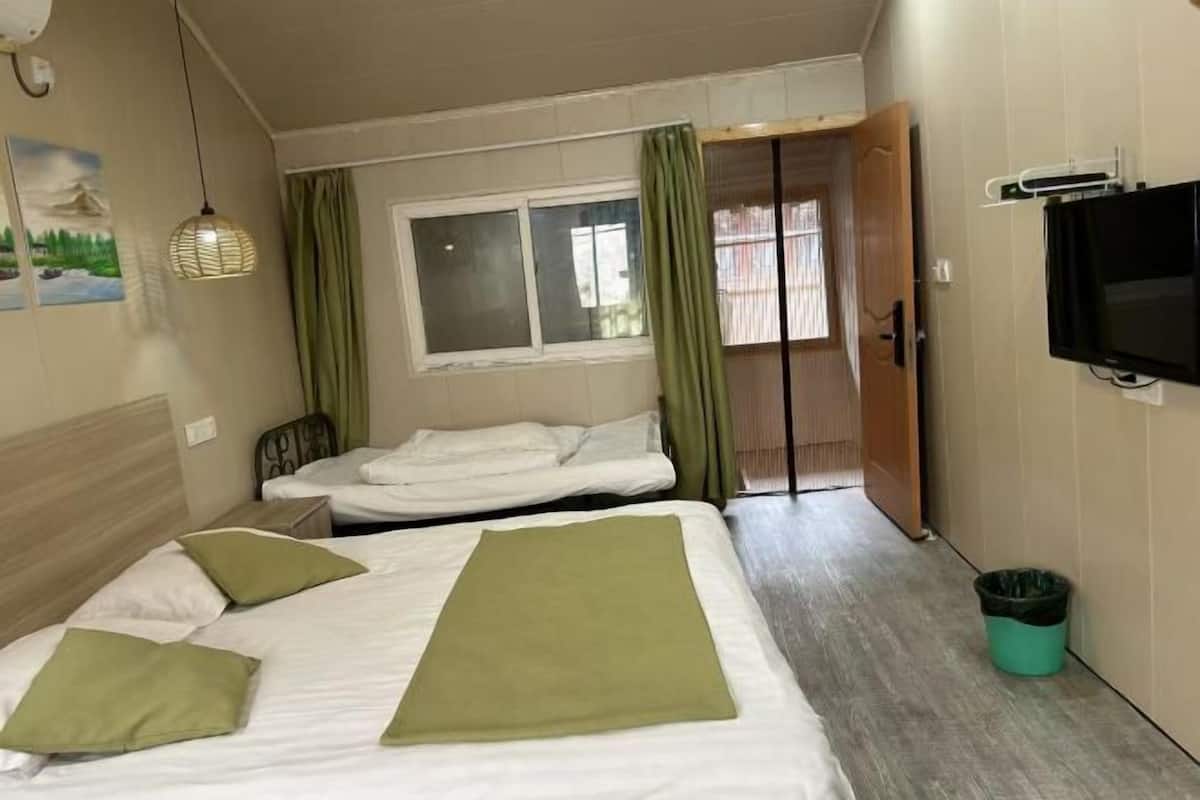 A hotel room with two beds, a television, a window with curtains, and a door leading to another room.