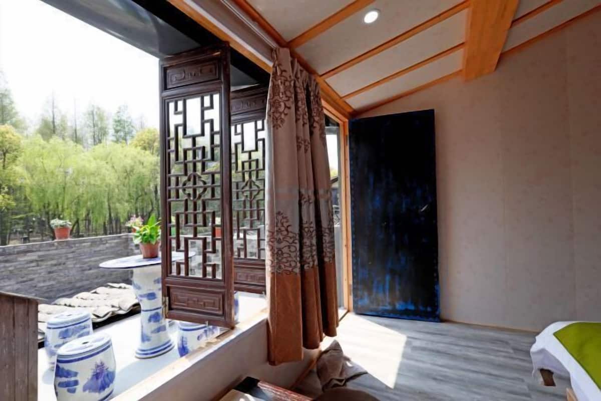A room with a large window, a decorative screen, and a view of greenery outside.