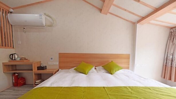 Un dormitorio con cabecera de madera, cama con ropa blanca y almohadas verdes, mesita de noche con hervidor y extintor rojo.