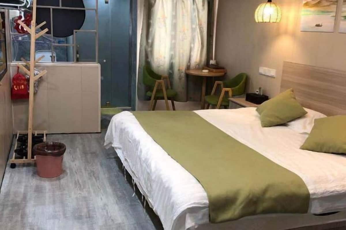 A hotel room with a bed, a small table, chairs, a trash bin, and a wall-mounted lamp.