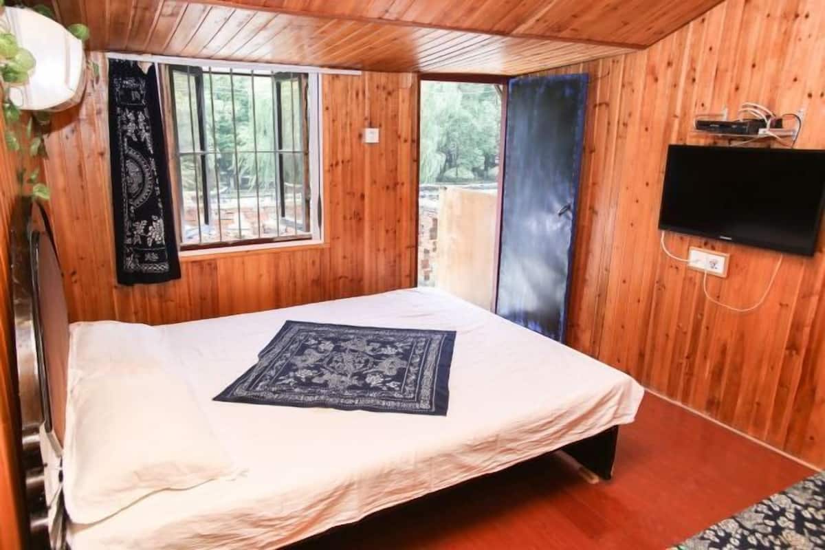 A wooden-paneled room with a bed, a window, a TV, and a view of the outdoors.