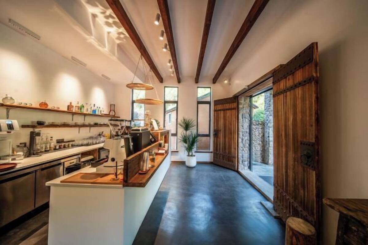 A modern kitchen with a central island, wooden beams, and a stone wall.
