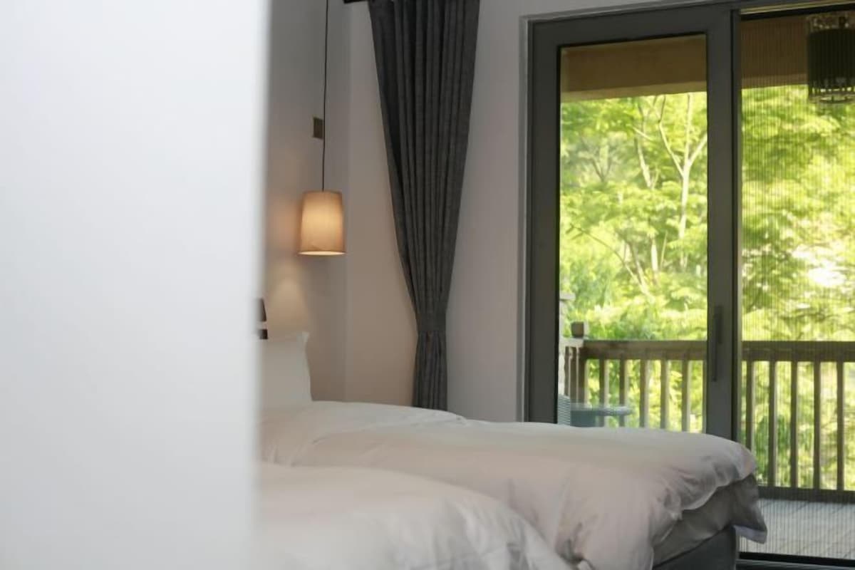 A bedroom with a large window, a bed, and a hanging light fixture.