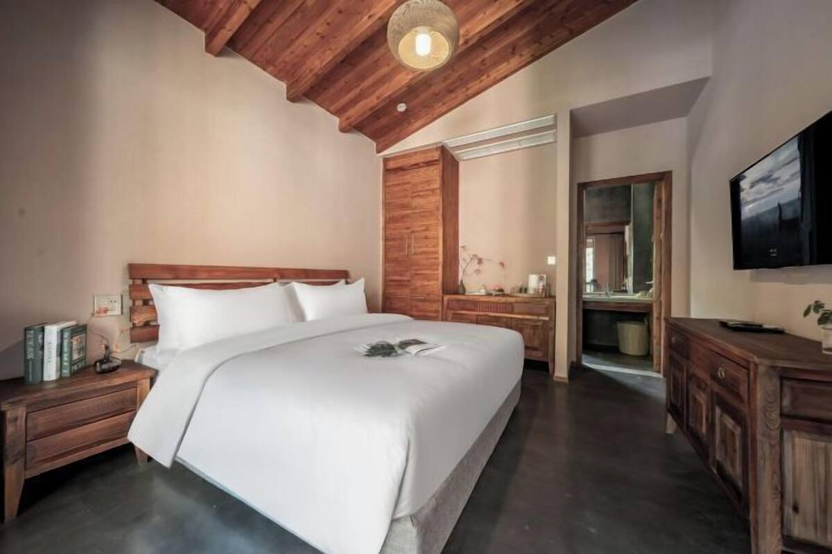 A bedroom with a wooden ceiling, a bed with white bedding, a wooden nightstand, a dresser, and a television on the wall.