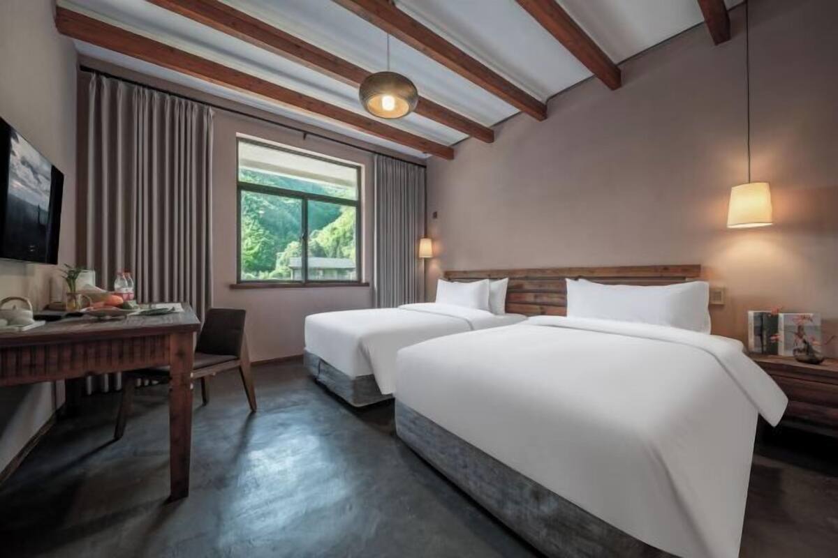 A hotel room with two beds, a desk, and a large window with curtains.