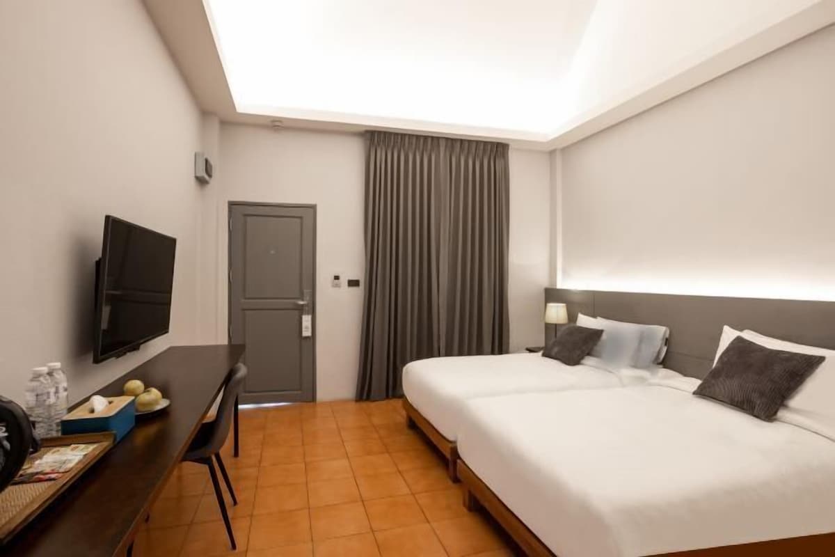 A hotel room with a bed, a desk with a TV, a door, and a window with curtains.