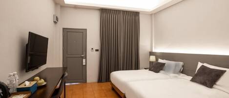 A hotel room with a bed, a desk with a TV, a door, and a window with curtains.