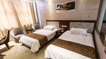 A hotel room with two beds, a sitting area with a chair, a small table, and a nightstand.