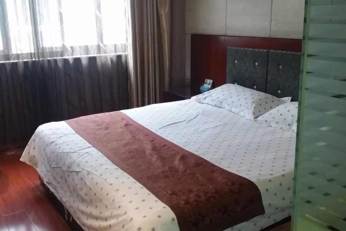 Een hotelkamer met een bed, gordijnen en een houten hoofdeinde.